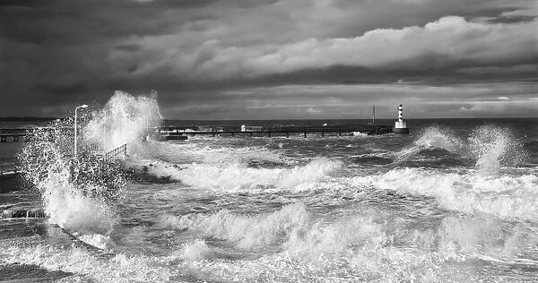 Waves Crashing Along The Coast With A Small Lighthouse At The End Of A Pier; Amble, Northumberland, England
