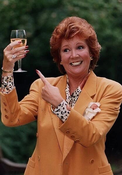 Cilla Black holding glass of wine wearing gold jacket and spotted blouse