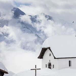 Clouds above the mountain huts and church covered with snow, Bettmeralp, district of Raron