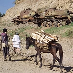 Horse carrying wood passes rusting tank from the war, Sentebe, Choa region