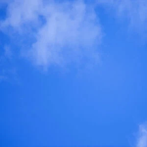 An airplane flies across a blue sky leaving vapour trails