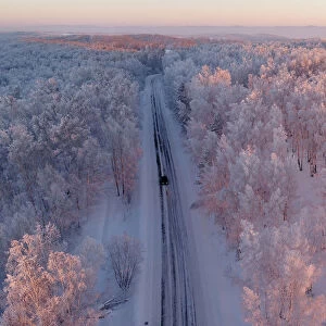 An aerial view shows a car driving along a forest road during sunset in the Siberian