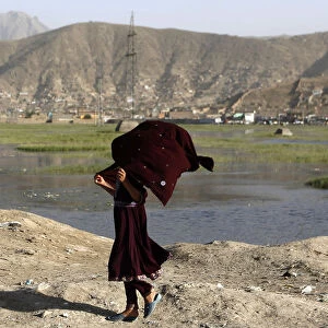 An Afghan girl holds on to her scarf as she walks down a road on a windy day in Kabul