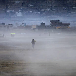 An Afghan man heads home walking through a dust cloud as the sun sets in Kabul