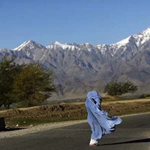 An Afghan woman in a burqa walks along a road on a windy day on the outskirts of Kabul