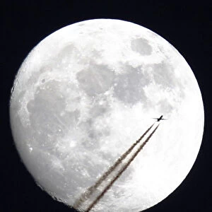 An aircraft passes in front of the moon above Manchester