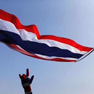 An anti-government protester gestures below a Thai national flag as he stands on a
