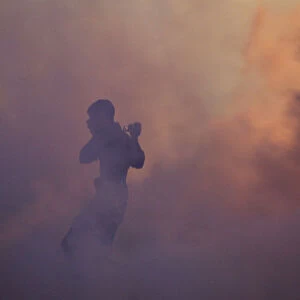An anti-government protester runs through a cloud of tear gas holding a camera during
