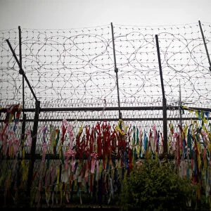 A barbed wire fence is decorated with ribbons bearing messages wishing for unification of