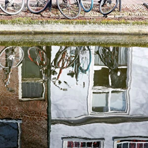 Bicycles are seen reflected in the water of a canal in Delft
