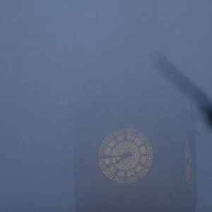 A bird flies past the Big Ben clock tower on a foggy morning in central London