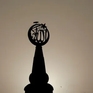 A bird sits on a religious sign on a mosque, silhouetted against the setting sun in A bird sits on a religious sign on a mosque, silhouetted against the setting sun in
