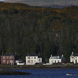A boat passes houses in Millport, Scotland