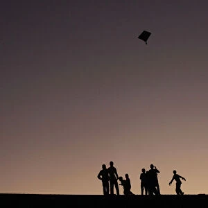 Boys are silhouetted against the setting sun as they fly a kite in Karachi