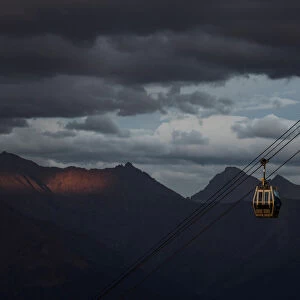 A cable car is pictured with Caucasus mountains during sunset in the background outside