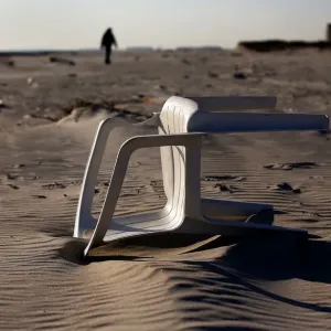 A chair is seen lying in the sand on the beach as a silhouette of a man walks in Atlantic