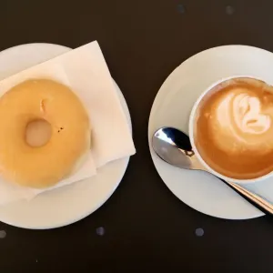 A coffee with milk and a donut are served in bakery in Vilassar de Dalt town A coffee with milk and a donut are served in bakery in Vilassar de Dalt town