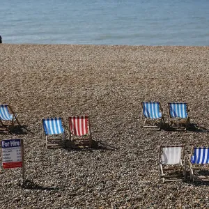 A couple sit on the beach near deck chairs in the sunny weather on Brighton beach A couple sit on the beach near deck chairs in the sunny weather on Brighton beach