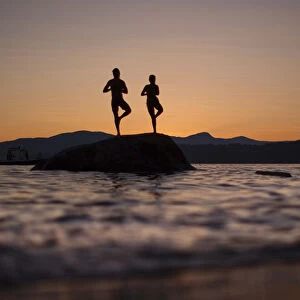 A couple stand on a rock facing the sunset along the shores of English Bay in Vancouver