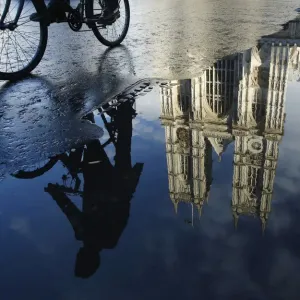 A cyclist is reflected in a puddle as he passes Westminster Abbey in London