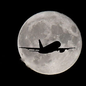 FILE PHOTO: A passenger plane passes in front of the full moon as it makes its final