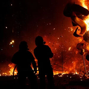Firemen observe figures of a monument as it burns during the finale of the Fallas