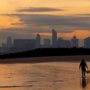 A fisherman digs for bait in front of the Liverpool skyline on the beach at New Brighton