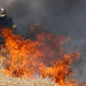 A French fireman uses a shovel behind flames in a burning field of barley during harvest