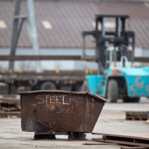 A garbage bin with the words STEEL MY JOB! painted on it sits in a storage yard where