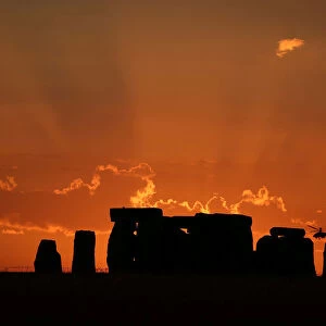 A helicopter flies behind the Stonehenge stone circle during sunset in southwest Britain