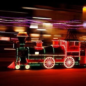 An illuminated tram in the shape of a steam locomotive passes under the illuminations