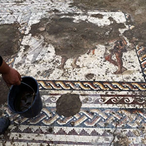 An Israel Antiquities Authority worker holds a bucket while cleaning a mosaic floor