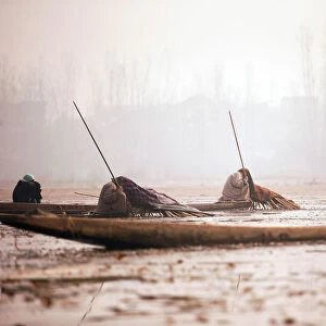 Kashmiri fishermen cover their heads and part of their boats with blankets and straw