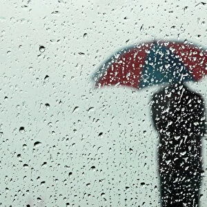 A man carrying an umbrella is seen silhouetted through a window covered with rain drops