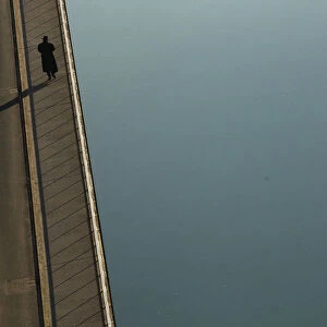 Man casts shadow as he walks along the shore of river Aare in Bern