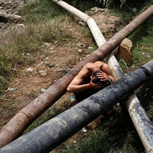 A man cools off near a leaking water pipeline, during hot and humid weather in Karachi