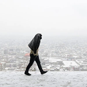 A man covers his head walks on a hilltop on a snowy day in Kabul, Afghanistan
