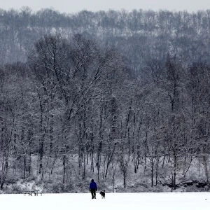 A man and dog walk in the falling snow in Rockland Lake State Park near the Hudson River