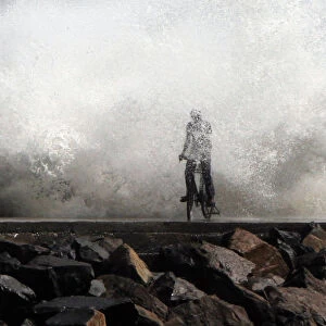 A man is drenched by a large wave during high tide as he cycles past at a fishing