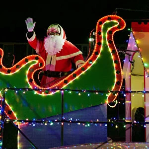 A man dressed as Santa Claus waves from a truck decorated in lights as it makes its