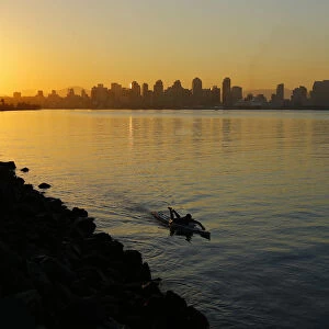 A man glides across the water on a paddle board as the sun rises in San Diego
