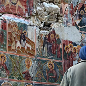 A man looks at a damaged fresco in The Orthodox Church of Saint Athanasios in Leshnica