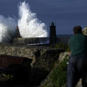A man looks at waves as they crash against a lighthouse in the port town of Viavelez