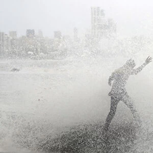 A man loses his balance as he gets drenched by a large wave during high tide at a