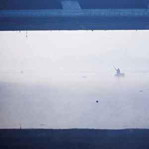 A man paddles a handmade boat across the Yamuna river on a foggy winter morning in