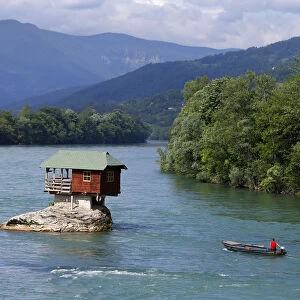 A man powers a boat near a house built on a rock on the river Drina near the western