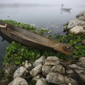A man pushes his boat with the help of a bamboo stick to reach the bank of Rapti River