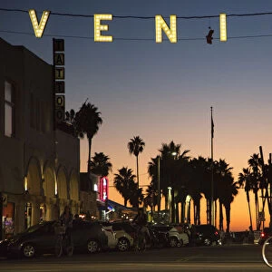 A man rides a bicycle under the Venice sign on Windward Avenue in Venice, California