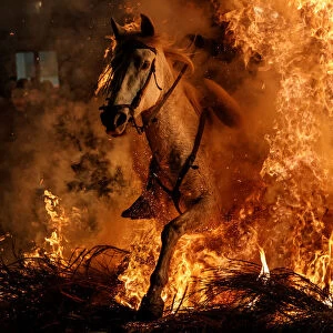 A man rides a horse through flames during the annual Luminarias celebration on the eve