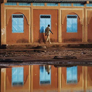 A man walking past a school is reflected in a large puddle in Niamey